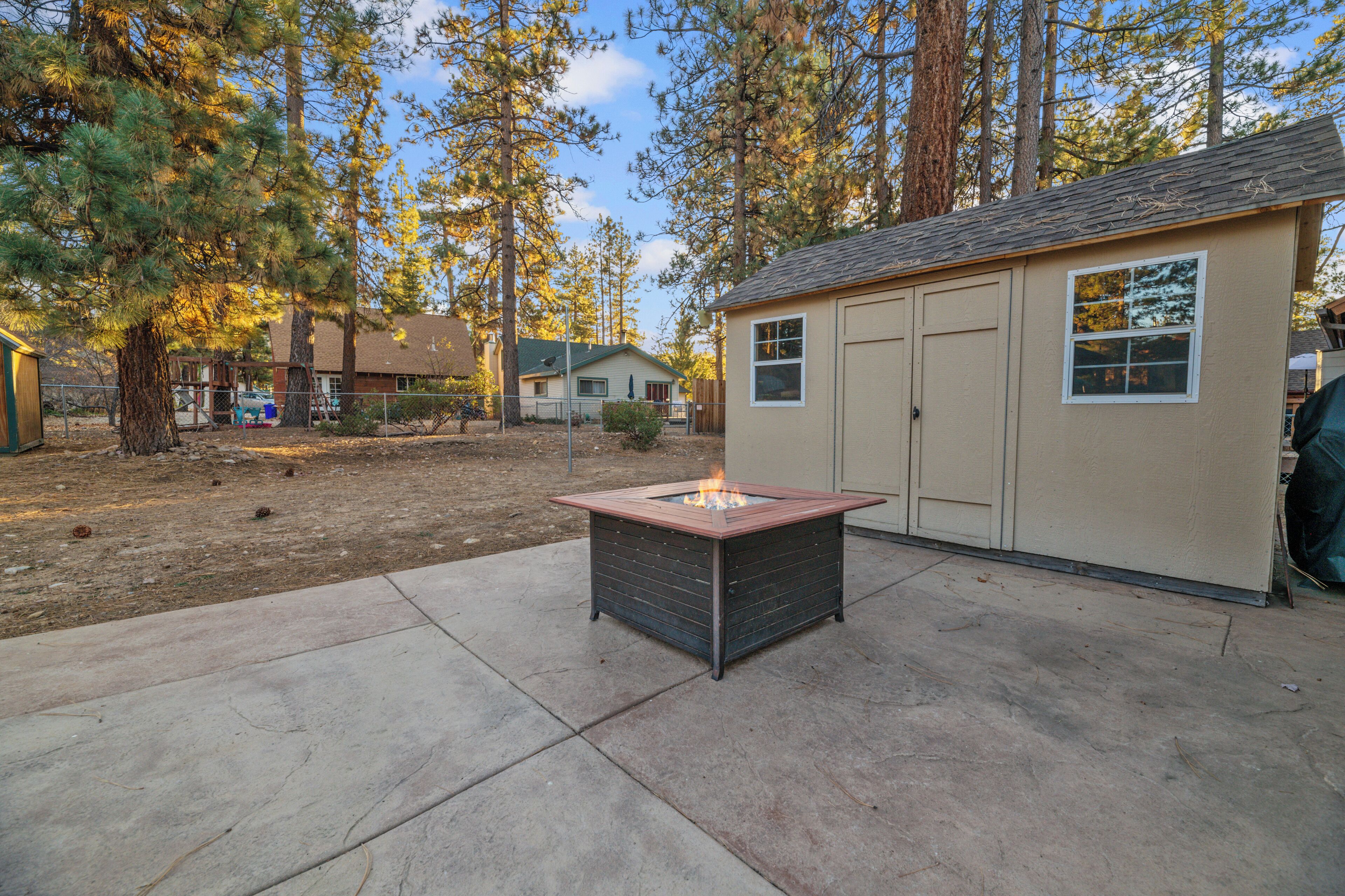 A square fire pit in a backyard with a shed and trees in the background.