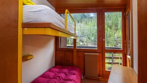 Een slaapkamer met stapelbedden en uitzicht op een bos door grote ramen.