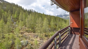 Een houten chalet met een balkon dat uitkijkt over een bebost berglandschap.