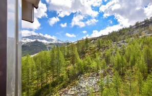 A mountainous landscape with dense green forests and snow-capped peaks under a partly cloudy sky.