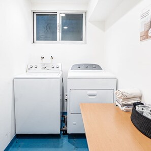 A laundry room with two washing machines, a dryer, and a table with folded clothes.