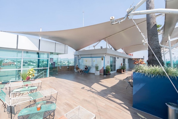A rooftop terrace with outdoor seating, a small building, and a view of the city.