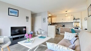 A modern living room with a flat-screen TV, a sofa, a coffee table with flowers, and a kitchen in the background. - A Deux Pas du Port - Vannes (VANNES)