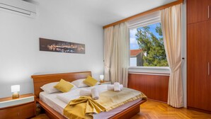 A hotel room with a wooden bed, a nightstand, a lamp, a window with curtains, a wardrobe, and a painting on the wall. - 4 bedroom amazing home in Zaboric (Zaboric)