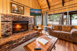 Una sala de estar acogedora con chimenea de ladrillo, piso de madera, un sofá y una mesa de centro.