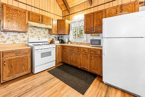 Una cocina con gabinetes de madera, estufa, microondas y refrigerador.