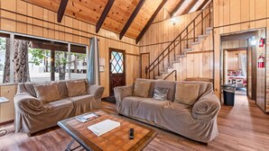 Interior acogedor de una cabaña de madera con dos sofás, una mesa de centro y una escalera.