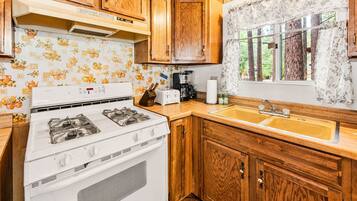 A kitchen with wooden cabinets, a white stove, a sink, and a window with curtains.