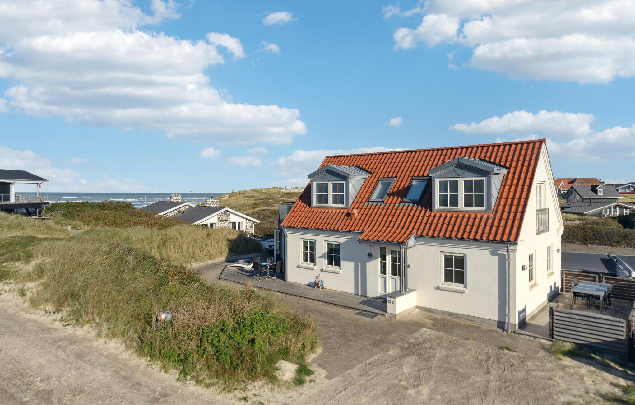 A coastal house with a red-tiled roof, two visible windows, and a paved driveway.