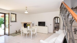 A spacious living room with a white sofa, a dining table with chairs, a fireplace, a TV, and a staircase. - 2 bedroom cozy home in Vasanello (Vasanello)