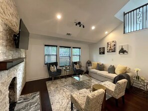 Uma sala de estar com lareira de pedra, dois sofás, uma mesa de centro e uma escadaria.