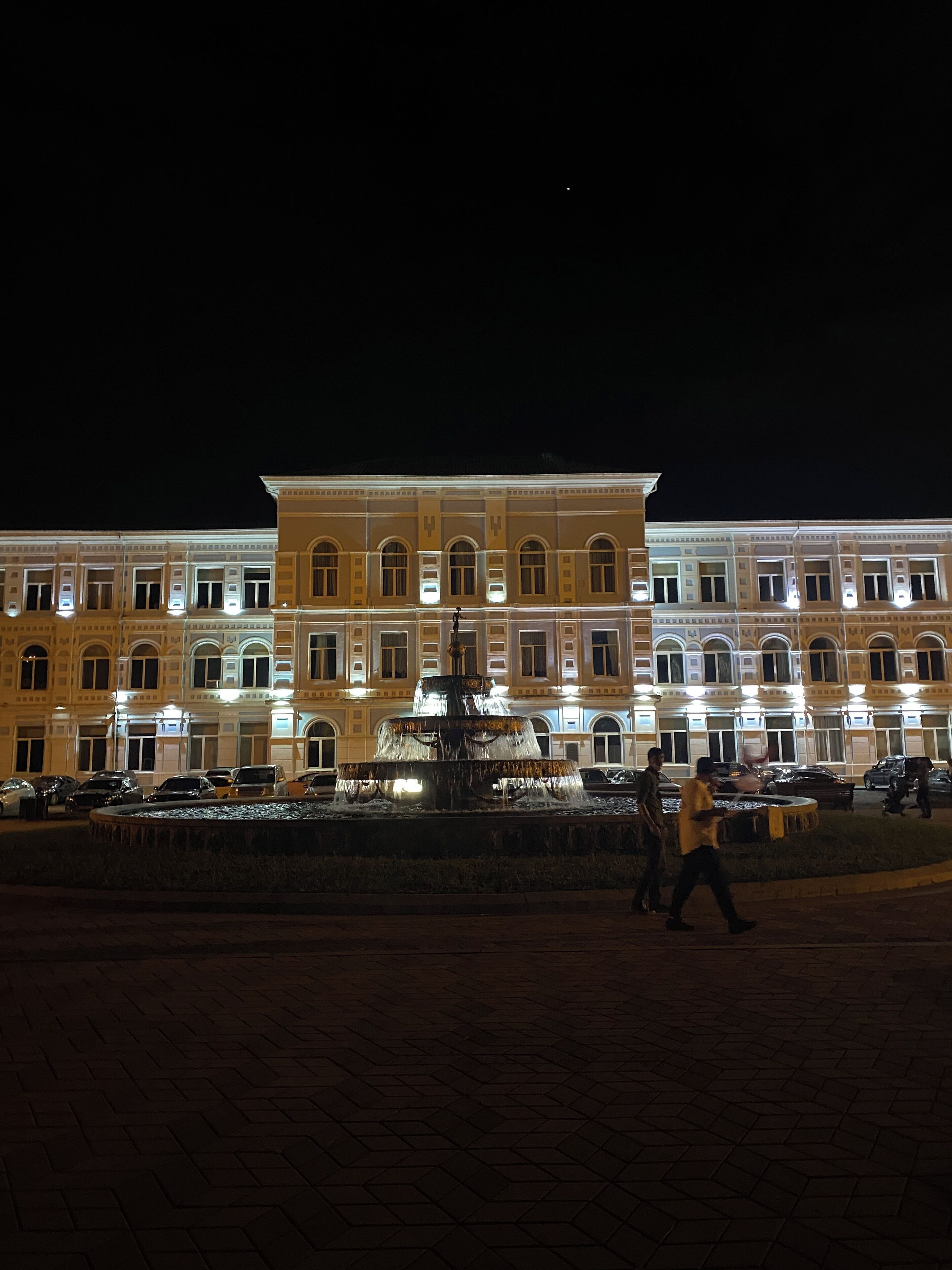 Um edifício com vários andares, uma fonte central e uma estátua.