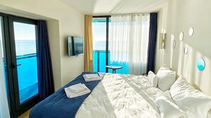 Een hotelkamer met een groot bed, een televisie, een tafeltje en uitzicht op zee.