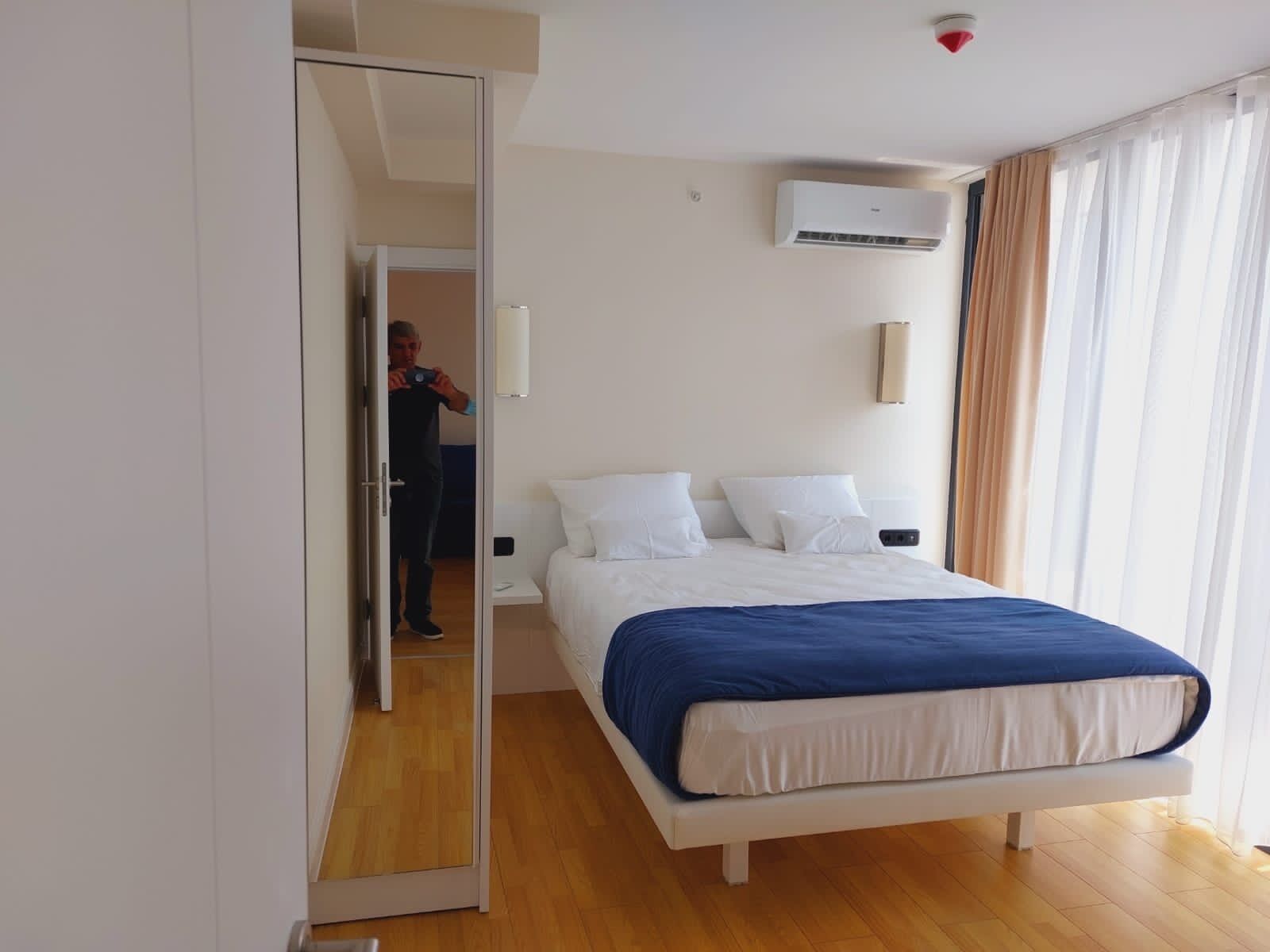 Una camera d'albergo con un letto, uno specchio, un condizionatore d'aria e vista su una persona all'esterno.