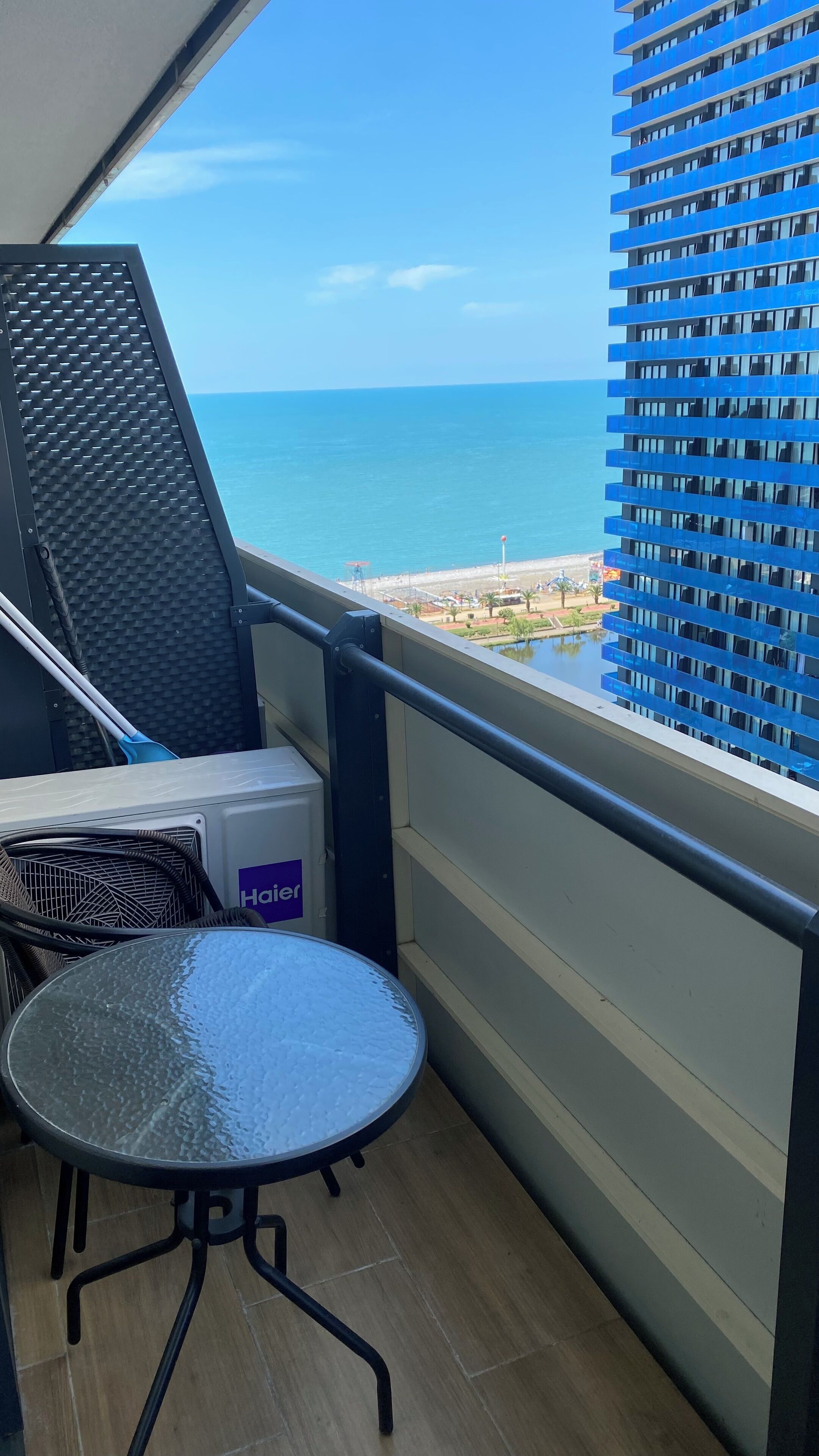 Un balcón con vista al mar, una mesa, sillas y un aire acondicionado Haier.