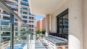 Een balkon met een bank, een glazen balustrade en uitzicht op andere gebouwen.