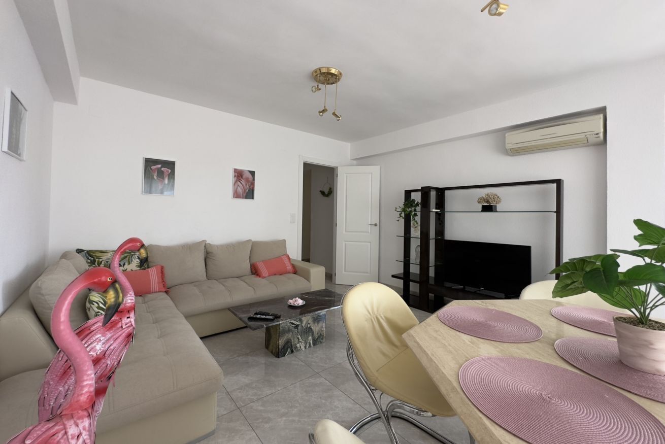 A modern living room with a sofa, coffee table, TV stand, and dining area.