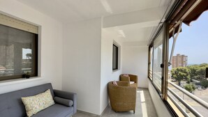Un balcon avec un canapé gris, un fauteuil en osier et une vue sur le paysage urbain.