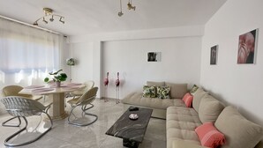 Un salon moderne avec une table à manger ronde, un canapé et une table basse. On y trouve deux chaises, une plante et un luminaire suspendu au plafond.
