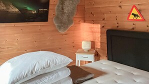 Habitación de cabaña de madera con cama, almohadas, mesita de noche, lámpara y un cartel de advertencia sobre alces en la pared.