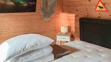 En stuga med träpanel, inredd med en säng, kuddar, ett nattduksbord, en lampa och en varningsskylt med en älg på väggen.