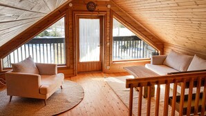 Un dormitorio acogedor en el ático con techo inclinado de madera, un ventanal grande, una puerta con cortinas, un sofá y una silla.