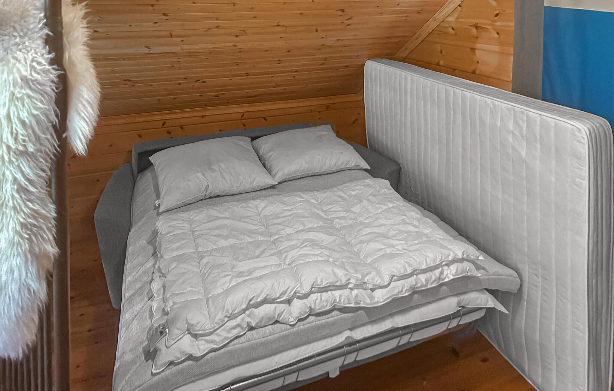 Un letto singolo con struttura grigia e biancheria da letto bianca in una stanza con pareti in legno e una testiera bianca.