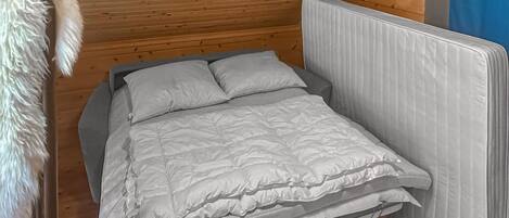 Un letto singolo con struttura grigia e biancheria da letto bianca in una stanza con pareti in legno e una testiera bianca.