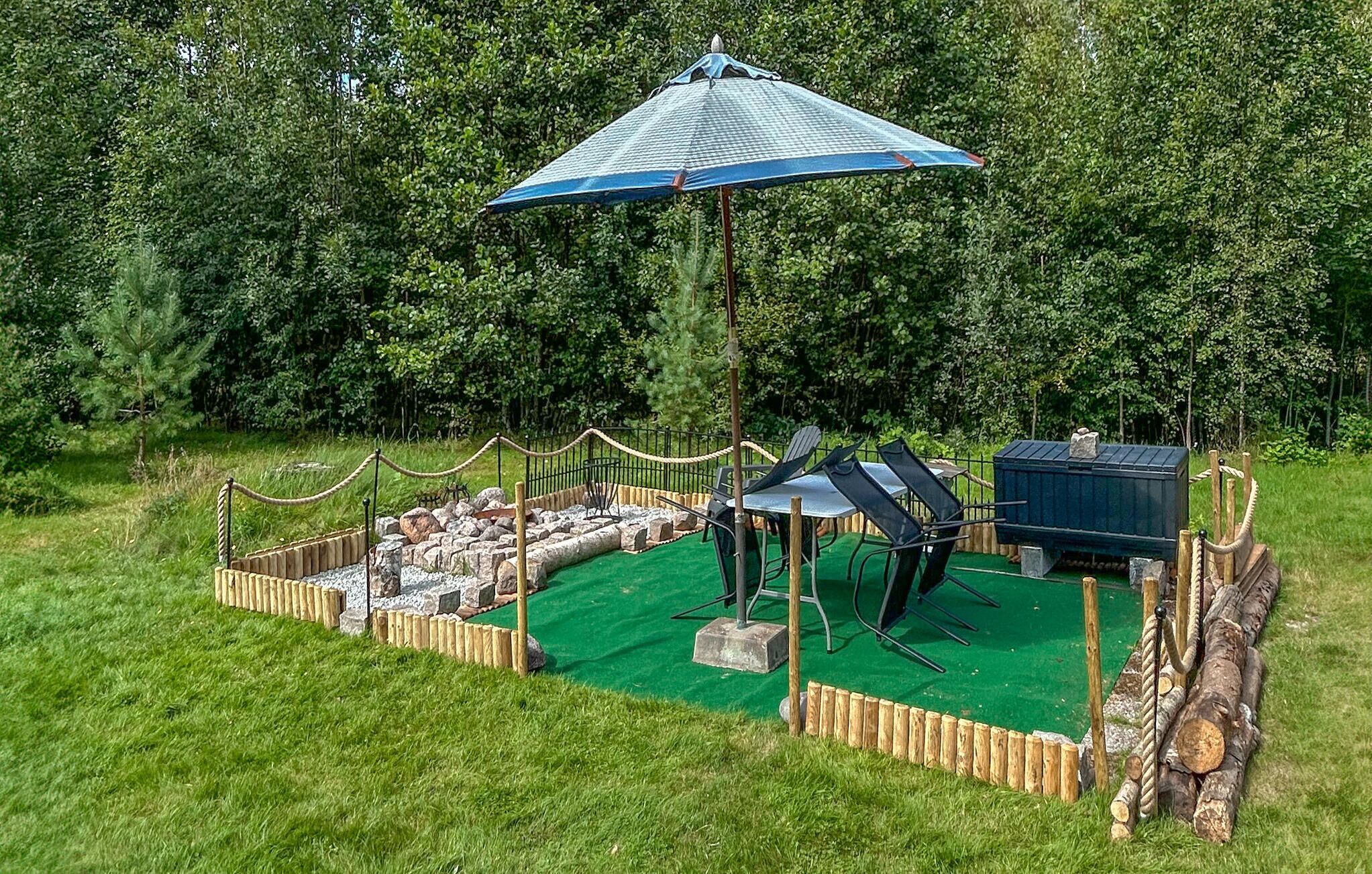 Een rustieke buitenruimte met groen kunstgras, een blauwe parasol en een houten omheining.
