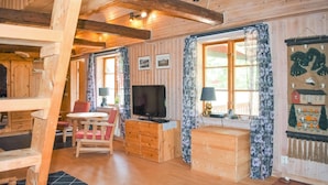 A cozy cabin interior with wooden walls, a TV, a wooden table with chairs, and a window with curtains. - Awesome home in Backaryd (Backaryd)