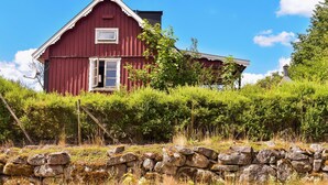 A red barn with a white window and door, surrounded by greenery and a stone wall. - Awesome home in Backaryd (Backaryd)