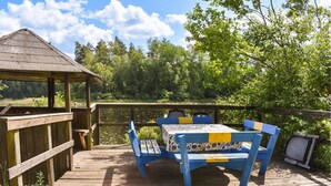 A wooden deck with a table and chairs, overlooking a body of water and surrounded by trees. - Awesome home in Backaryd (Backaryd)