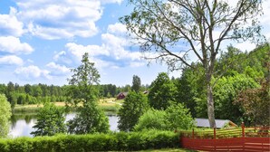 A serene lakeside setting with a red fence, lush greenery, and a small building in the background. - Awesome home in Backaryd (Backaryd)