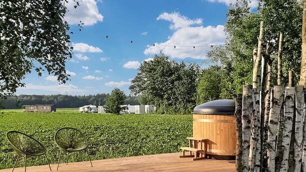 En træterrasse med to stole, en sauna og udsigt over et grønt græsareal og landbrugsbygninger.
