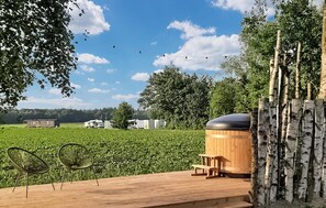 A wooden deck with two chairs, a sauna, and a view of a green field and farm buildings. - Nice apartment in Schoonloo with WiFi (Schoonloo)