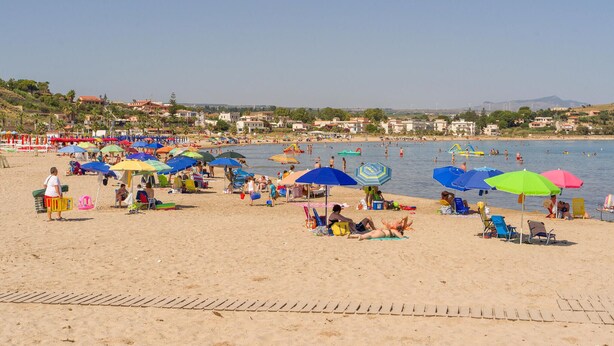 Ein Strand mit vielen bunten Sonnenschirmen und Menschen, die im Sand entspannen.