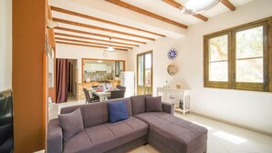 Ein Wohnzimmer mit einer Couch, ein Essbereich mit Tisch und Stühlen, eine durch eine offene Tür sichtbare Küche und ein großes Fenster mit Blick.