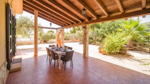 Eine überdachte Terrasse mit Esstisch, umgeben von Steinpfeilern und Topfpflanzen.