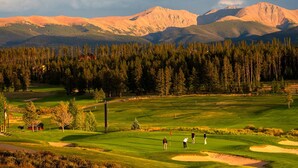 Golfkenttä, jonka taustalla kohoavat vuoret, ja jossa on hiekkabunkkereita sekä lipunvarsi.
