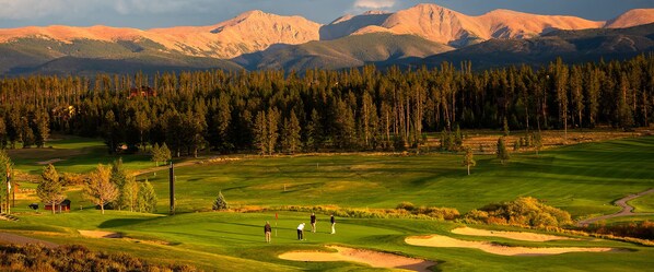 A golf course with a mountainous backdrop, sand bunkers, and a flagstick.