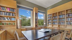 Een bibliotheek met boekenkasten, een schaakbord en uitzicht op bomen door grote ramen.