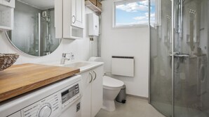 Kompakti ja moderni kylpyhuone, jossa on puinen allaskaappi, wc ja lasiseinällä varustettu suihku.
