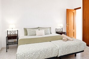 Una cama bien hecha con una colcha estampada, dos mesitas de noche con lámparas y una puerta de madera.