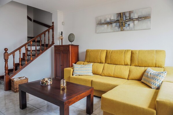 Una sala de estar con un sofá amarillo, una mesa de centro de madera y una escalera.