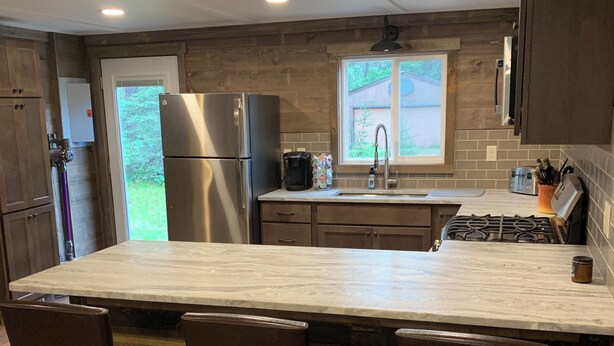 A modern kitchen with a large island, wooden cabinets, stainless steel appliances, and a window providing natural light. - Minutes to town or very peaceful woods retreat! Close to trails and golf. (Lewiston)