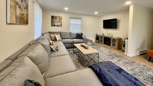 Un salon moderne avec un canapé d’angle, une table basse et un téléviseur à écran plat fixé au mur.