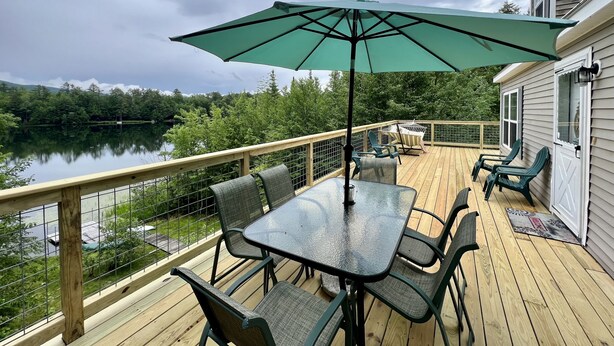 Une terrasse en bois avec une table et des chaises, offrant une vue sur un lac et une forêt.