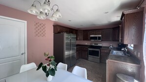 Eine moderne Küche mit Edelstahlgeräten, Holzschränken und einem Essbereich mit weißem Tisch und Stühlen.