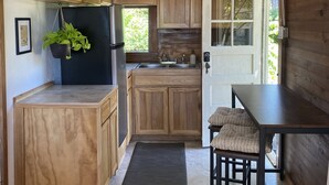 A compact kitchen with wooden cabinets, a black refrigerator, a sink, and a dining area with a table and chairs. - Cozy Cottage near Bigfork overlooking Flathead Lake in our Cherry Orchard (Bigfork)