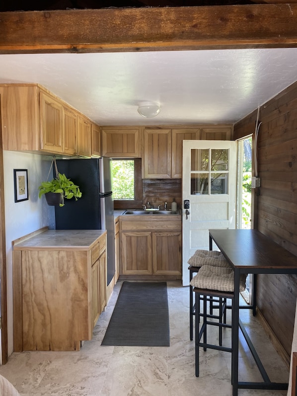 A compact kitchen with wooden cabinets, a black refrigerator, a sink, and a dining area with a table and chairs.